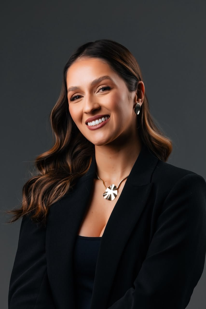Dra. Mariana Tezza sorrindo, de blazer preto, em retrato de estúdio
