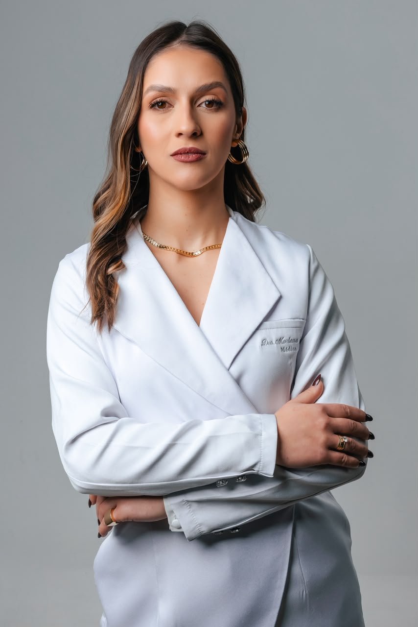 Dra. Mariana Tezza de jaleco branco bordado, braços cruzados