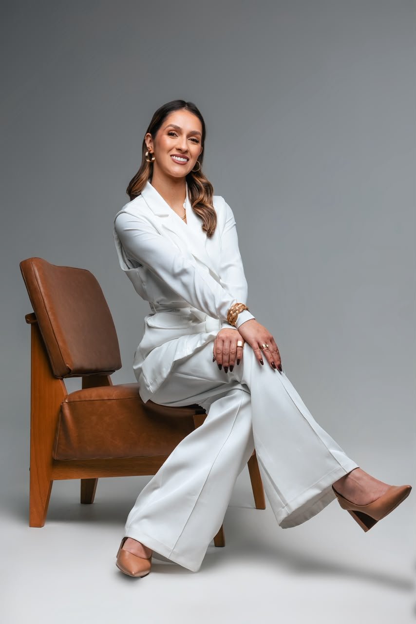 Dra. Mariana Tezza sentada em uma poltrona de couro, sorrindo, vestindo terno branco